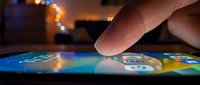 Finger touching illuminated smartphone screen with bokeh lights in background, representing mobile technology interaction and digital communication.