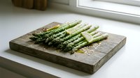 Fresh green asparagus spears with sea salt on rustic wooden cutting board by kitchen window for healthy cooking and meal preparation.