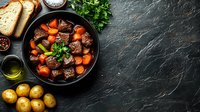 Hearty beef stew with tender meat chunks, carrots and herbs in cast iron pan, served with bread and potatoes on dark stone background.