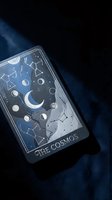 Mystical tarot card The Cosmos featuring celestial moon phases, constellations and stars on dark blue fabric background for spiritual divination readings.