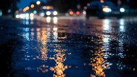 Wet city street at night with glowing bokeh lights reflecting on rain-soaked asphalt, creating a moody urban atmosphere.