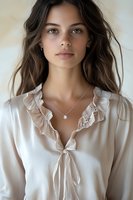 Young woman with natural makeup wearing white silk blouse with ruffle collar and delicate necklace. Long brown hair frames face with light eyes and neutral expression.