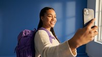 Young African American female student with backpack taking selfie with smartphone in modern university hallway, smiling happily for social media content.