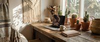 Cozy boho home office workspace with rustic wooden desk, laptop, cacti in terracotta pots, macrame wall decor, and warm natural sunlight.