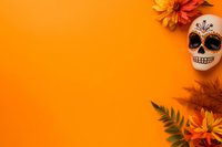 Mexican sugar skull with orange dahlia flowers and fern leaves arranged on vibrant orange background, creating festive Day of the Dead composition with copy space.
