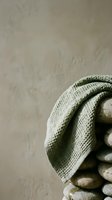 Folded linen cloth draped over stacked smooth stones against neutral textured background, suitable for spa, wellness, and minimalist design projects.