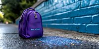 Purple backpack on asphalt ground against blue brick wall background with shallow depth of field and bokeh effect, back to school concept for education and study.