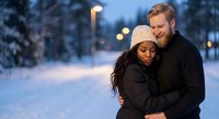 Young interracial couple embracing in snowy winter evening with warm street lights creating romantic atmosphere for holiday season and love concepts.