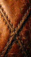 Aged brown leather texture with crossed stitching seams showing natural grain and weathered patina for luxury craftsmanship and vintage material backgrounds.