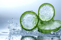 Fresh cucumber slices with water droplets and splash on light background, macro photography showing crisp texture and natural freshness of organic produce.
