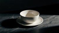 Minimalist ceramic cup and saucer set on dark textured surface, featuring clean lines and neutral tones for contemporary home decor and tableware design projects.
