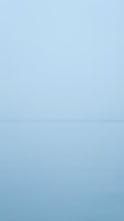 Serene seascape with calm waters meeting a misty horizon under soft blue sky, conveying tranquility and minimalist coastal aesthetics for backgrounds and design projects.