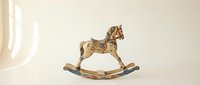 Vintage wooden rocking horse with hand-painted floral details and worn patina, displayed on a light background, evoking nostalgia and childhood charm.