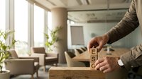 Businessman stacking wooden blocks spelling PEOPLE in modern office environment representing human resources management and team building concepts.
