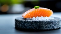 Fresh salmon nigiri sushi piece on black stone plate with crushed ice and micro herbs garnish, selective focus on vibrant orange fish texture. Perfect for menu design.
