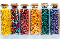 Colorful pharmaceutical pills and capsules in glass bottles arranged in rainbow order on white background. Medical supplies and pharmacy concept.