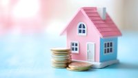 Pink miniature house model with stack of gold coins on pastel blue background, representing real estate investment, mortgage, and home savings concept.