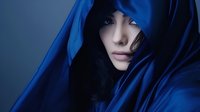 Young Asian woman with long dark hair wrapped in deep blue silk fabric against dark background, creating mysterious and dramatic portrait with ethereal lighting.