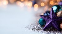 Glittering purple star decoration with teal and copper ornaments against blurred golden bokeh background creates magical holiday atmosphere.