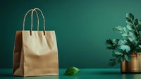 Kraft paper shopping bag on emerald green background with decorative plant in gold pot, minimalist eco-friendly retail mockup for branding and design.