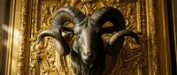 Ornate goat head sculpture with curved horns mounted on golden decorative wall panel, featuring intricate baroque-style carved details and luxurious gold leaf embellishments.