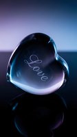 Crystal glass heart with engraved Love inscription glowing in blue and purple light, reflecting on dark surface for romantic Valentine's Day designs.