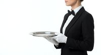 Professional waiter in black tuxedo and bow tie holding silver serving tray, hospitality service concept isolated on white background for restaurant design.