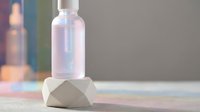 Clear glass bottle with dropper cap on geometric concrete block, minimalist skincare and cosmetics product display for branding and packaging design.