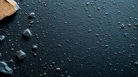 Dark textured surface with scattered rock fragments and water droplets creating dramatic contrast against deep blue-black background for atmospheric design projects.