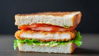 Fresh club sandwich with crispy bacon, lettuce and tomato on toasted bread served on wooden table against dark background for restaurant menu design.