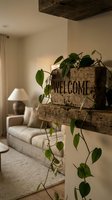 Rustic wooden welcome sign with trailing green ivy on a shelf, cozy living room with neutral sofa and warm lamp light in background.