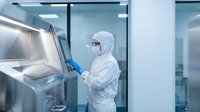 Laboratory technician in protective cleanroom suit operating advanced equipment in sterile pharmaceutical manufacturing facility for research and development.