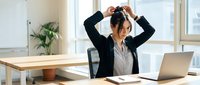 Young Asian businesswoman stretching arms above head during work break at modern office desk with laptop for stress relief and workplace wellness.
