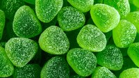 Green sugar-coated gummy candies in close-up view, showing texture and crystalline surface for food photography and confectionery marketing.