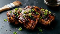Grilled pork ribs with glossy barbecue glaze, sesame seeds and green onions on dark slate surface. Smoky barbecue cuisine for restaurant menus and cooking blogs.