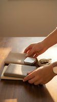 Woman hands organizing beige leather accessories wallet purse and jewelry on wooden table in warm natural sunlight for lifestyle photography.