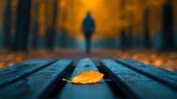 Solitary yellow autumn leaf on wooden bench with blurred silhouette of person walking in foggy park during golden sunset creating moody atmosphere.
