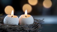 Glowing white textured tea light candles nestled in twigs with soft bokeh lights in background create peaceful spa or meditation atmosphere.