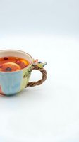 Whimsical ceramic mug with bird handle detail filled with hot tea and floating berries, isolated on white background for design projects and beverage concepts.