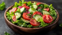 Fresh garden salad with sliced tomatoes, cucumbers and lettuce in rustic wooden bowl on dark background, healthy vegetarian meal with seasonal ingredients.