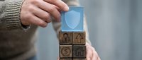 Man in sweater stacking wooden blocks with insurance icons including shield, car, health, money and house symbols for protection concept.