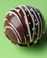Dark chocolate truffle decorated with white chocolate stripes and silver sugar crystals on green background. Close up macro food photography.