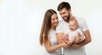 Happy young Caucasian family with newborn baby smiling together in white clothing against neutral background for parenting and family lifestyle content.