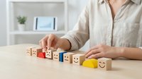 Professional woman arranging wooden blocks with emoji faces and star rating symbols on desk for customer satisfaction feedback concept.