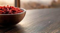 Dried red goji berries in wooden bowl on dark rustic table with natural lighting, superfood and healthy eating concept for wellness lifestyle.