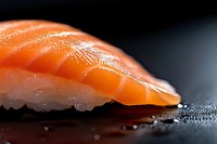 Fresh salmon nigiri sushi with glistening orange fish slice on seasoned rice, showcasing traditional Japanese cuisine preparation on dark surface.