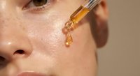 Woman applying facial serum with dropper for skincare routine. Golden oil treatment for hydration and anti-aging. Natural beauty and wellness concept.