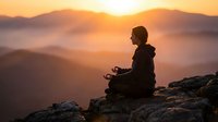 Person meditating on mountain peak at sunrise with golden light and misty valleys below creating peaceful spiritual atmosphere for wellness content.