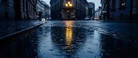 Wet urban street at dusk with rain-soaked pavement reflecting streetlights and buildings, creating moody atmosphere for weather, city, and atmospheric design projects.