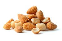 Fresh whole and cracked almonds scattered on white background, isolated macro shot showing natural texture and detail of raw nuts for healthy eating concept.
